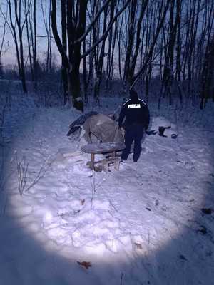 Policjant przed namiotem rozbitym w zagajniku leśnym na śniegu