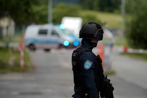 Policjant w hełmie kevlarowym a w tle stojący policyjny radiowóz