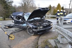 Zniszczone bmw widok z przodu i prawej strony. Na zdjęciu po prawe strażacy i policyjny radiowóz oraz widoczne uszkodzenia metalowych elementów drogowych