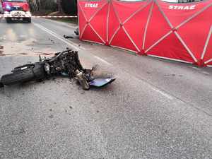 zniszczony motocykl leżący na drodze asfaltowej, czerwona płachta strazy pożarnej zasłaniajaca miejsce