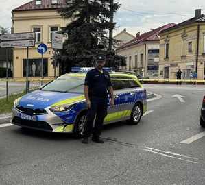 Oznakowany radiowóz na miejscu zdarzenie i żółta policyjna taśma odzielająca to miejsce, przed nim umundurowany policjant.