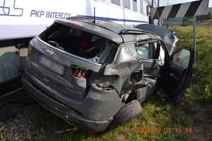 Zniszczony Jeep stojący obok torów kolejowych, za nim wagon pociągu Intercity.