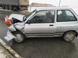 Zbliżenie na zniszczenia samochodu kia, widok z lewej strony. W tle naczepa ciężarówki