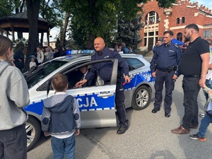Policjanci rozmawiający z lokalną społecznością i demonstrujący radiowóz  policyjny