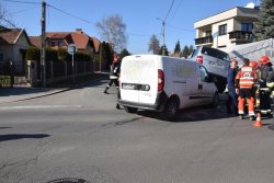 Zbliżenia na kolizję pojazdów fiata i volkswagena, który tylną osią stoi na pokrywie silnika fiata. Obok grupa osób w ubraniu cywilnym oraz umundurowaniu strażackim oraz ratownika medycznego.