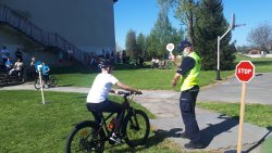 Uczestnik w trakcie praktycznego egzaminu na kartę rowerową. Umundurowany policjant z policyjnym lizakiem podaje wskazówki dla rowerzysty