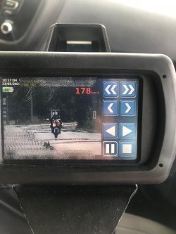 Zdjęcie ręcznego miernika prędkości na który jest obraz motocyklisty i wyświetlona jest prawym górnym roku jego prędkość 178 km na godzinę. Zdjęcie miernika zrobione jest w samochodzie.