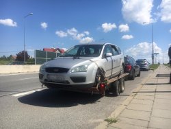 Srebrny ford stojący na przyczepie - lawecie tyłem do holującego samochodu, za nim granatowe auto i samochód policyjny