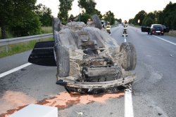 samochód osobowy marki BMW leży na dachu na drodze, widoczny proszek neutralizujący oleje i płyny