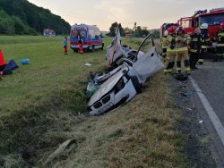 Białe BMW z rozciętym dachem w rowie melioracyjnym, na drodze dwa samochody strażackie, obok nich strażacy