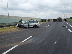 Zniszczony samochód osobowy na pasie autostrady przy barierach oddzielających pasy ruchu.