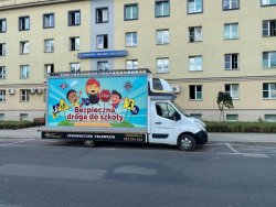 Samochód dostawczy stojący na parkingu przed budynkiem KMP w Tarnowie z reklamą bezpiecznej drogi do szkoły