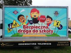 Baner reklamowy &amp;quot;Bezpieczna Droga do szkoły&amp;quot; widoczne uśmiechnięte rysunki dzieci oraz znaki drogowe informujące o dzieciach rowerzystach. Z prawej strony logo Komendy Miejskiej Policji w Tarnowie z lewej znaczek ruchu drogowego &quot;R&quot;