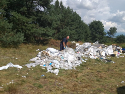 Umundurowany policjant przeszukuje stertę odpadów utworzoną na polanie