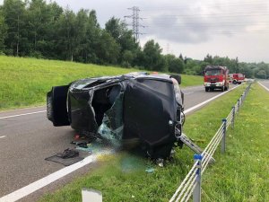 Zniszczone bmw leżące na prawym boku, z tyłu widoczne wozy strażackie