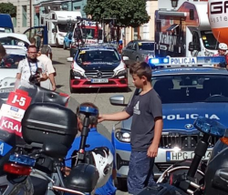 Chłopiec oglądający motocykle. Na pierwszym planie kufry motocykli policyjnych w tle oznakowany radiowóz i samochód Mercedes jednej z grup kolarskich wyścigu