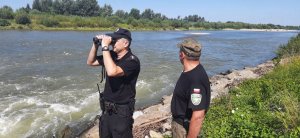 Podczas patrolu policjant używa lornetki obserwując drugi brzeg rzeki