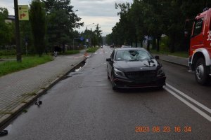 czarny samochód osobowy stoi na drodze, w samochodzie rozbita przednia szyba, po prawej stronie wóz strażacki