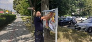 dzielnicowy zawiesza na tablicy miejskiej plakat przestrzegający seniorów przed oszustami