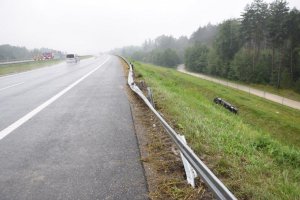 Zniszczona bariera energochłonna, ciemny samochód osobowy leży na boku w rowie melioracyjnym