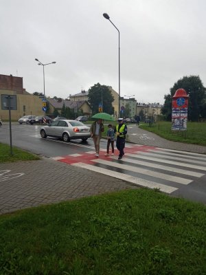 Policjant przechodzi przez przejście dla pieszych z dzieckiem i jego opiekunem