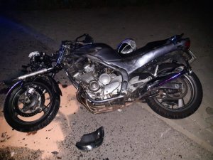 Motocykl leżący na prawej stronie na jezdni, dookoła rozsypany piasek neutralizujący oleje i paliwa