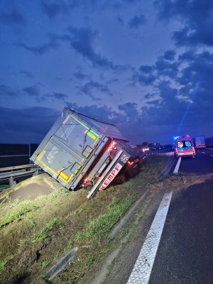 Samochód ciężarowy przewrócony na lewą stronę na pasie zieleni, po prawej stronie karetka pogotowia