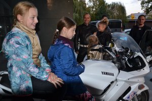Dzieci na motocyklu policyjnym. W tle umundurowany policjant w stroju motocyklowym, obok uczestnicy oglądający pojazd