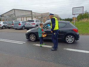 Policjant ruchu drogowego podczas kontroli pojazdu, obok stoi dziecko w owocami