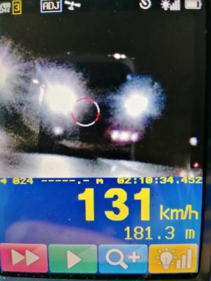 Zdjęcie z ręcznego miernika prędkości pokazujące ciemny pojazd jadący w nocy z włączonymi przednimi światłami mijania. Poniżej wskazana prędkość 131 km na godzinę.
