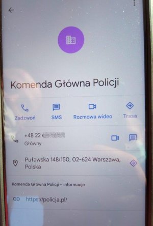 Wyświetlacz telefonu komórkowego z nazwą wyświetlaną Komenda Główna Policji w Warszawie numerem telefonu adresem KGP oraz adresem strony interentowej