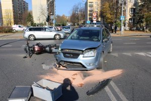 Srebrny ford z uszkodzoną prawą stroną pokrywą silnika, obok leży motocykl, przed samochodem rozsypany piasek neutralizujący oleje i paliwo