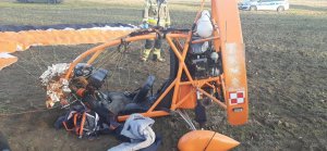 Motoparalotnia z rozłożonym, leżącym na ziemi spadochronem, z tylu stoi strażak