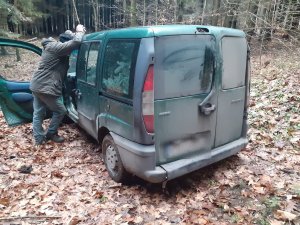 Zielony samochód Fiat Doblo, przed którym stoi mężczyzna obrócony bokiem. W samochodzie widoczne gałęzie jodłowe