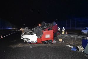 Leżący na dachu czerwony Volkswagen Transporter z białym przednim zderzakiem. Wokół rozrzucone bagaże. Zdjęcie wykonane w porze nocnej