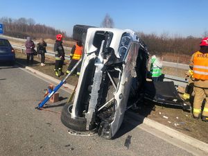 Uszkodzony samochód osobowy leżący na lewym boku, dookoła strażacy