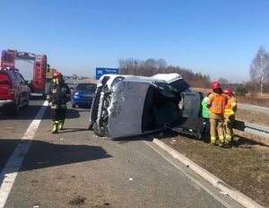 Biały samochód osobowy leżący na lewym boku, dookoła strażacy