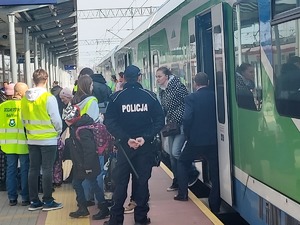 Policjant strzeże bezp9iecześńtwa osób przyjeżdżających na tarnowski dworzec PKP. Wśród uchodźców wolontariusze.