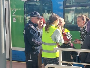 Umundurowany policjant oraz wolontariusze pomagający uchodźcom z Ukrainy, którzy przyjechali na dworzec PKP