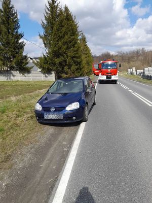 Niebieski samochód volkswagen stojący na poboczu. Z tyłu samochód straży pożarnej. Pora dzienna