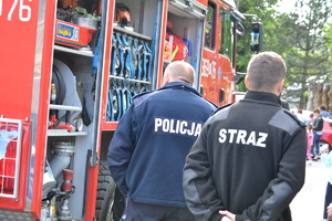 strażak i policjant stoją tyłem obok wozu strażackiego