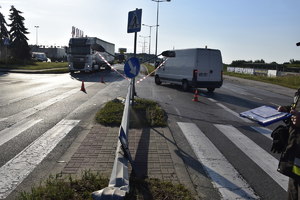 Przewrócona latarnia uliczna. Widoczne przejście dla pieszych i ruch pojazdów po drodze w obu kierunkach.