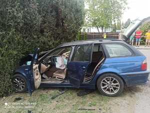Niebieski samochód stojący z rozbitym przodem przy żywopłocie
