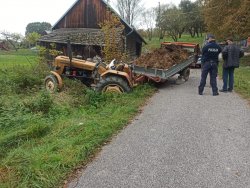 Widok ogólny ciągnika rolniczego i przyczepy. Na drodze widoczny policjant i osoba cywilna