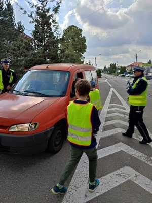 Dzieci w kamizelkach odblaskowych podczas kontroli samochód wraz z umundurowanymi policjantami