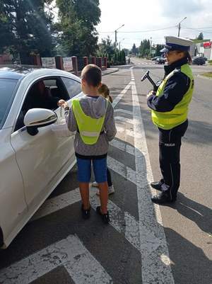 Dzieci w kamizelkach odblaskowych podczas kontroli samochód wraz z umundurowanymi policjantami