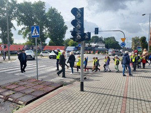 Grupa przedszkolaków z policjantem ruchu rogowego podczas przechodzenia przez przejście dla pieszych.