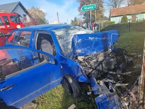 Uszkodzony przód niebieskiego samochodu osobowego, z tyłu widoczny znak z napisem NIWKA 2
