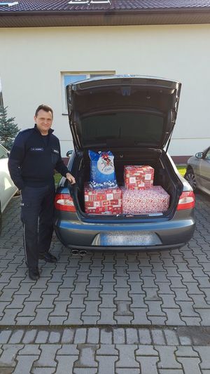 Policjant przy samochodzie w którym znajdują się świąteczne paczki