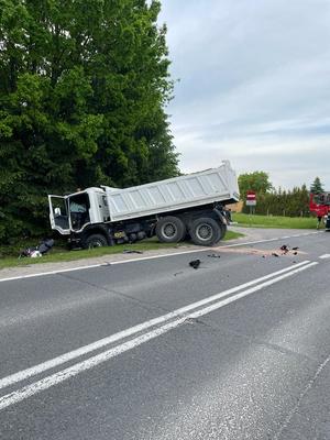 Ogólny widok miejsca wypadku. W oddali widać samochód ciężarowy i motocykl w rowie melioracyjnym, a bok częściowo wóz straży pożarnej.